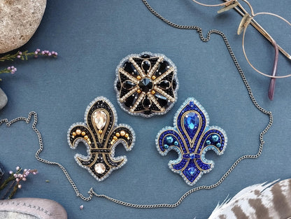 three ornate brooches with intricate designs and sparkling gemstones, arranged on a blue background.