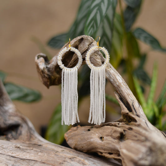 a pair of white tasseled earrings hanging from a tree branch