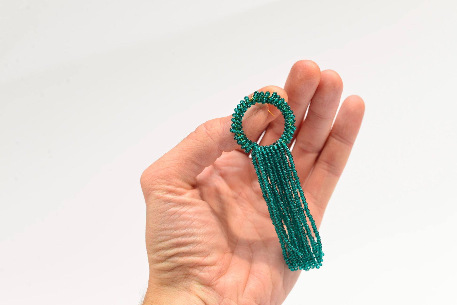 a hand holding a green beaded ring