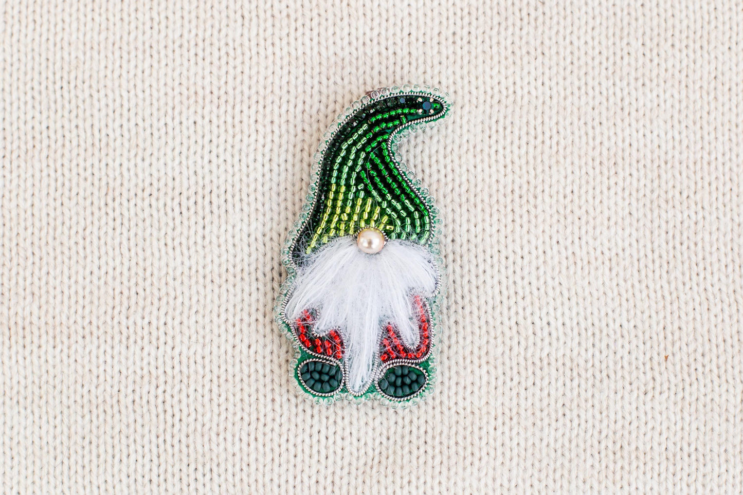 A colorful, hand-made ornament resembling a gnome or gnome-like figure, made of beads and featuring a white beard and red and green accents.
