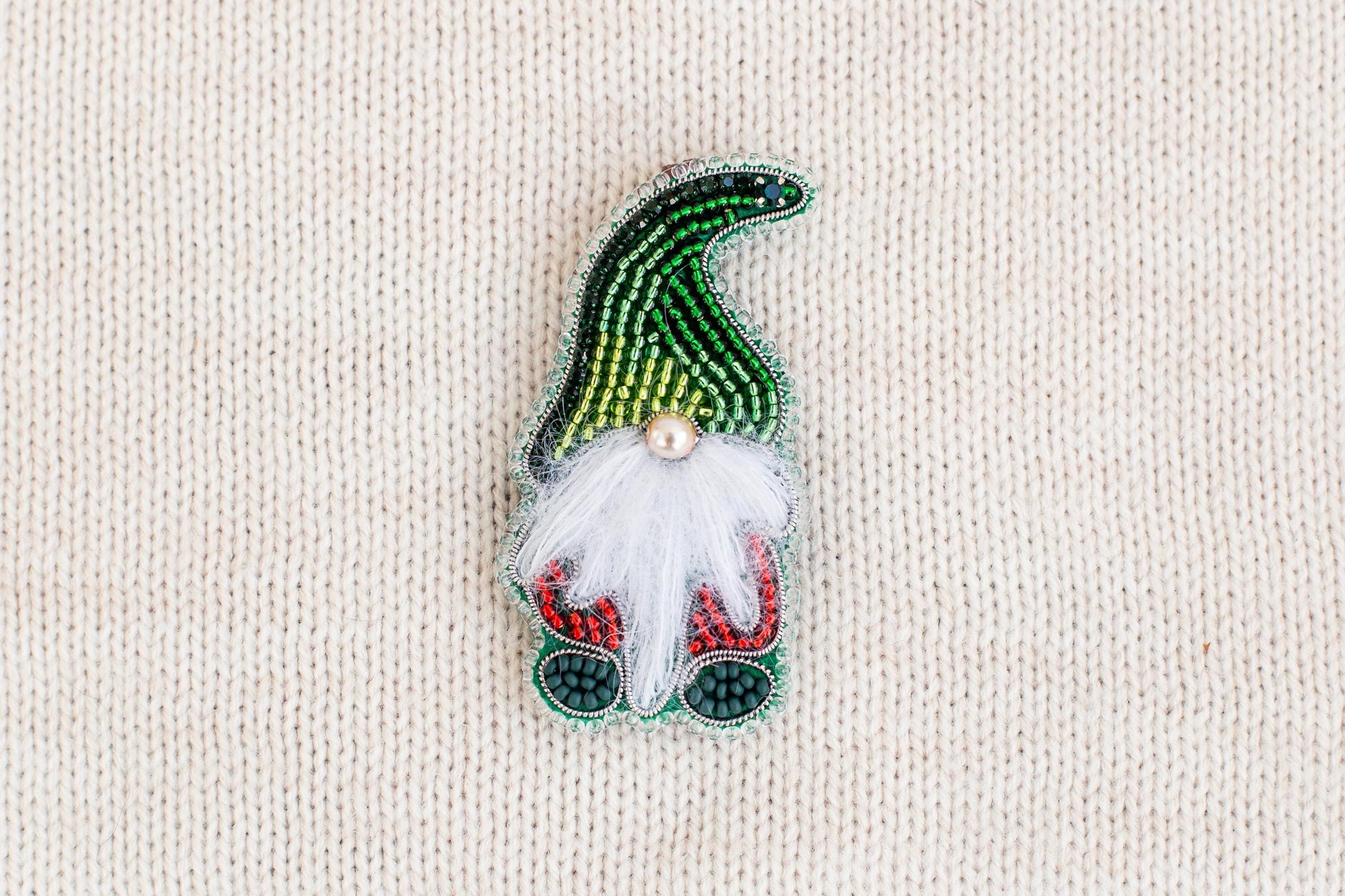 A colorful, hand-made ornament resembling a gnome or gnome-like figure, made of beads and featuring a white beard and red and green accents.