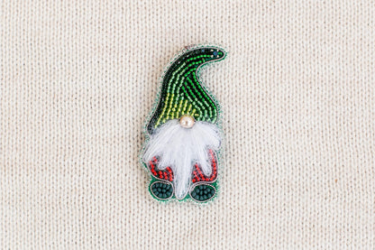 A colorful, hand-made ornament resembling a gnome or gnome-like figure, made of beads and featuring a white beard and red and green accents.