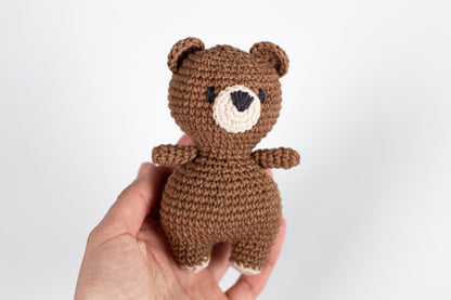 a hand holding a small crocheted teddy bear