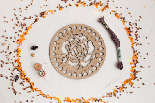 a wooden clock with a rose on it surrounded by beads and thread