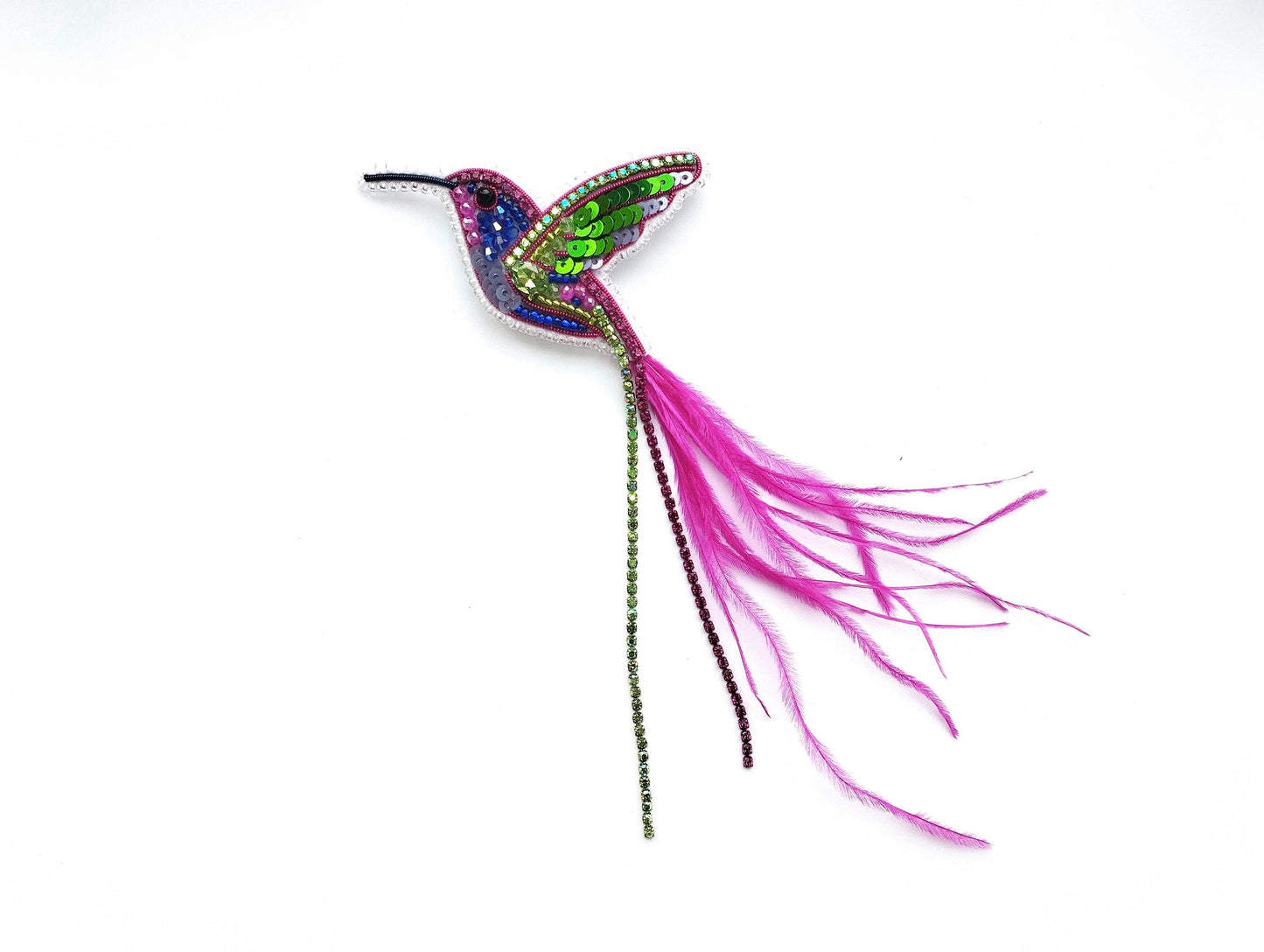 A colorful, sparkling hummingbird brooch with a long pink feather tail.