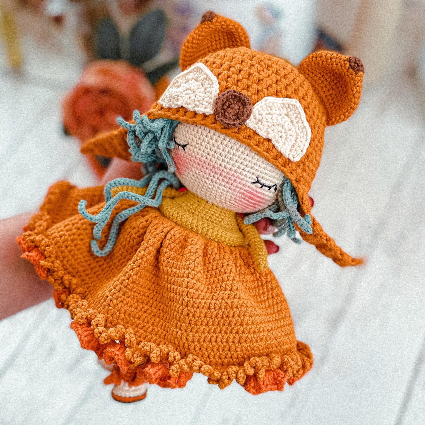 a hand holding a crocheted doll in a dress