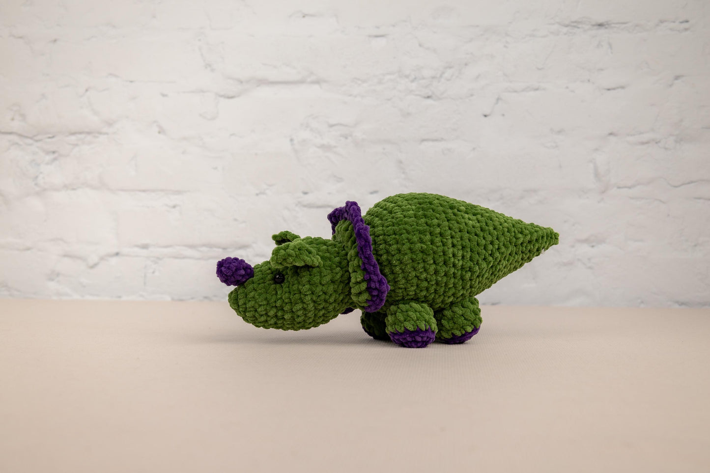 a green crocheted stuffed animal with a purple ribbon around its neck