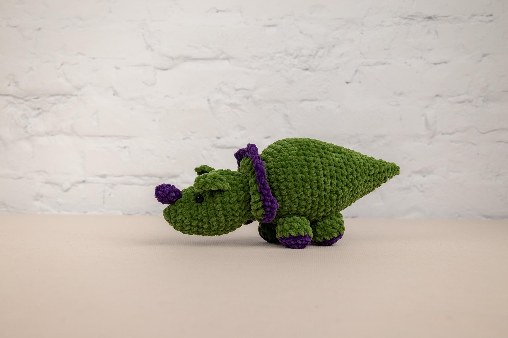 a green crocheted stuffed animal with a purple ribbon around its neck