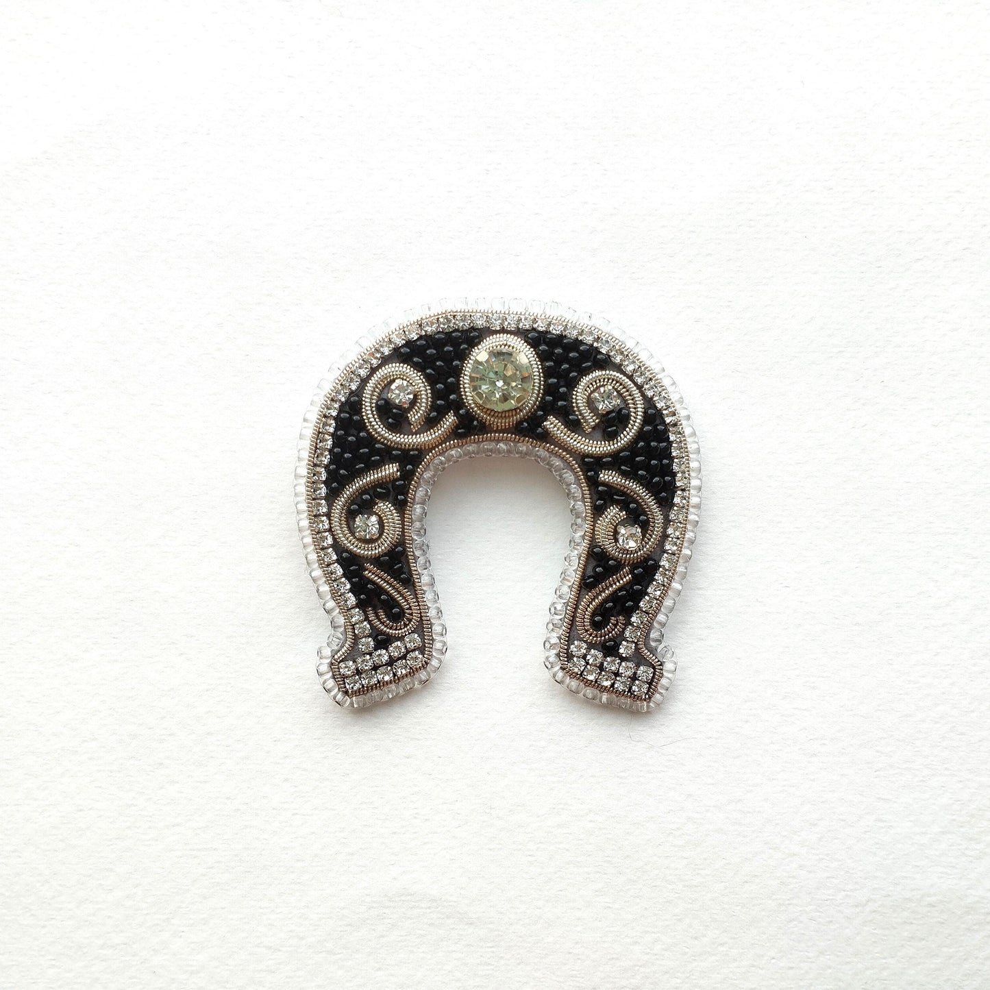A decorative horseshoe-shaped object with a central stone and intricate beading and embroidery around the edges.