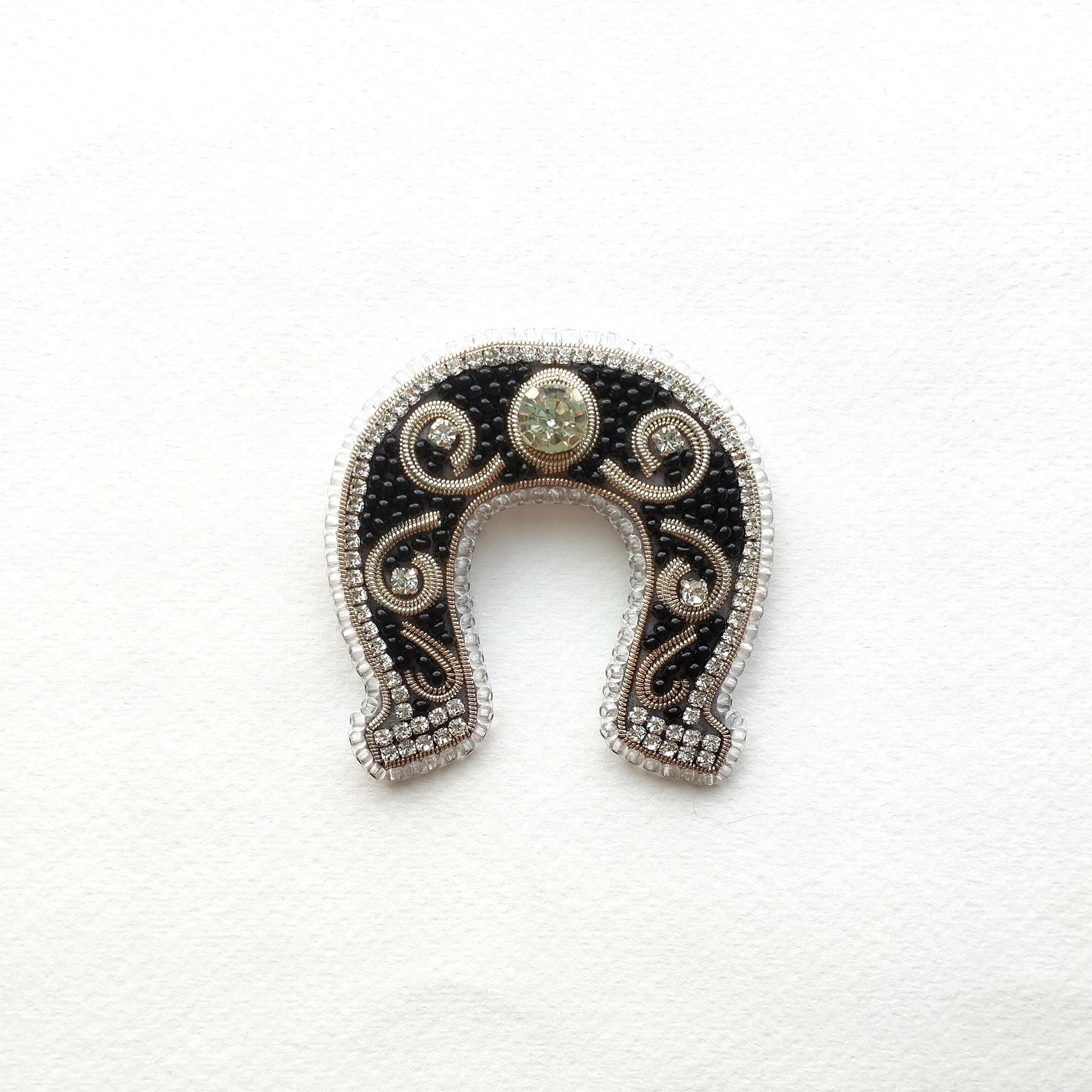 A decorative horseshoe-shaped object with a central stone and intricate beading and embroidery around the edges.