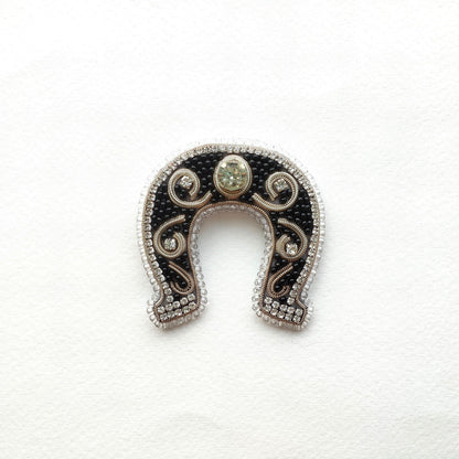 A decorative horseshoe-shaped object with a central stone and intricate beading and embroidery around the edges.