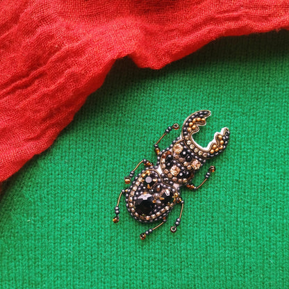 A decorative brooch in the shape of a beetle, adorned with jewels and beads, is displayed on a green fabric surface.