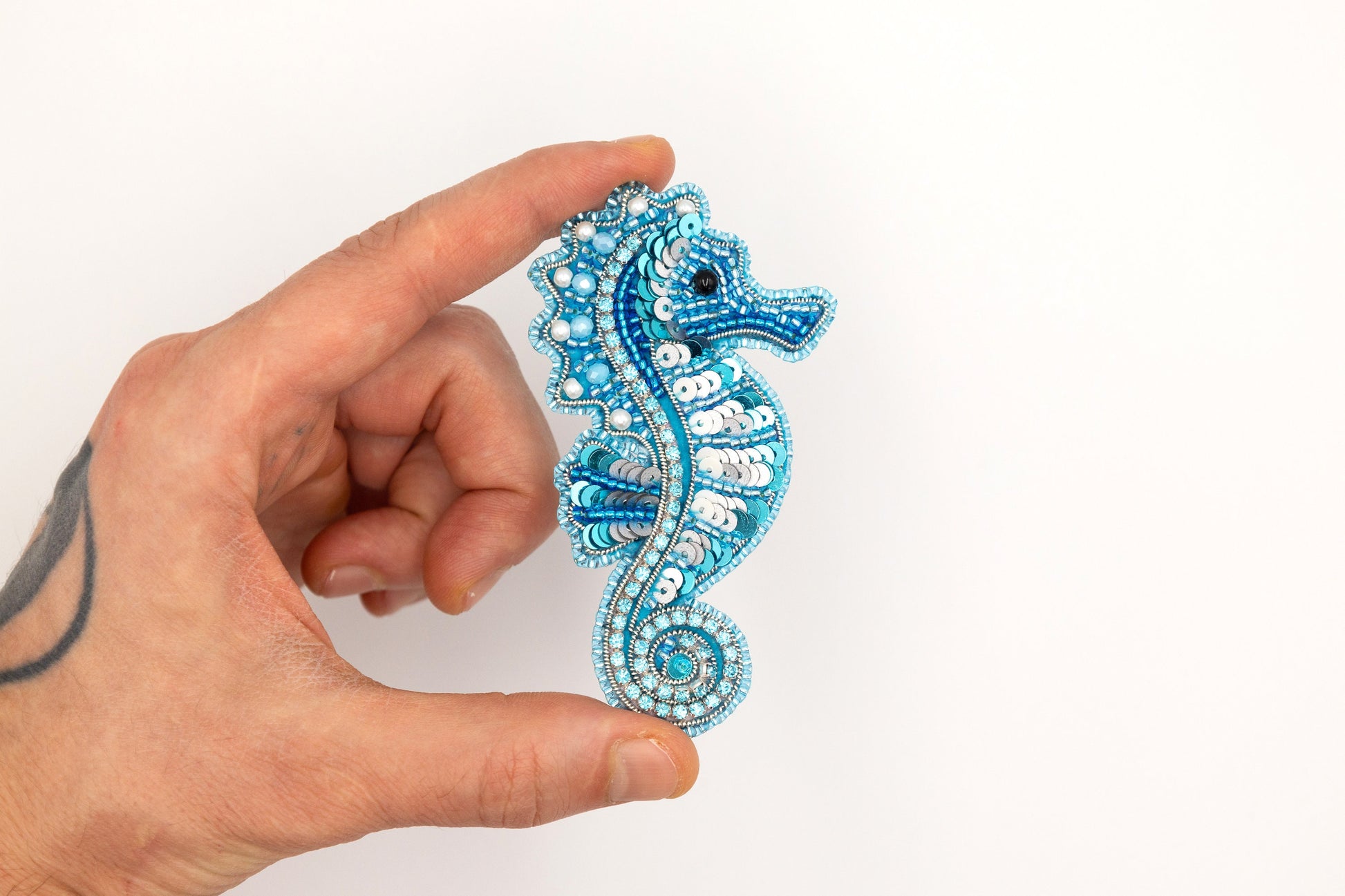 a hand holding a blue beaded seahorse brooch