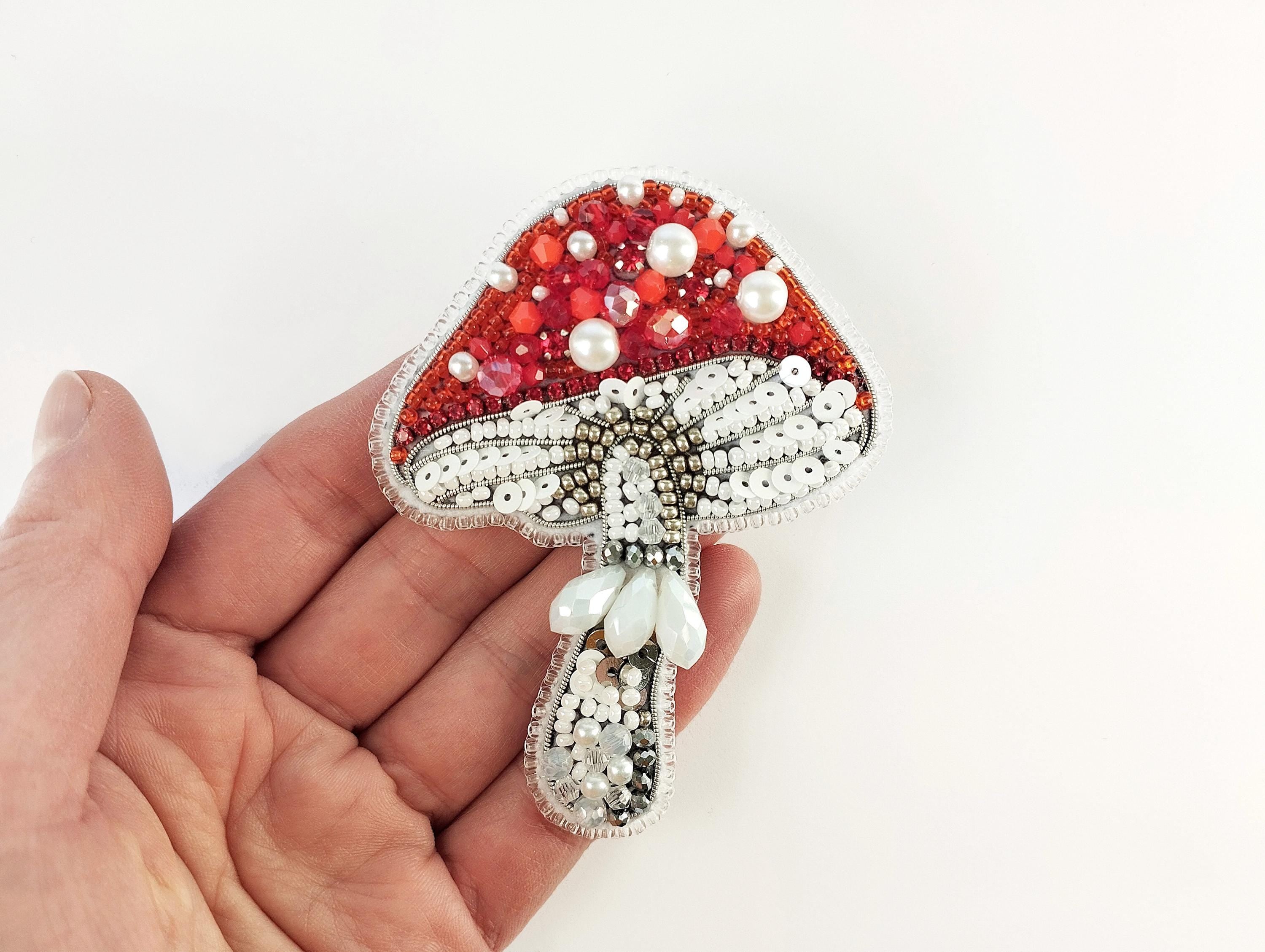 a hand holding a red and white brooch with pearls