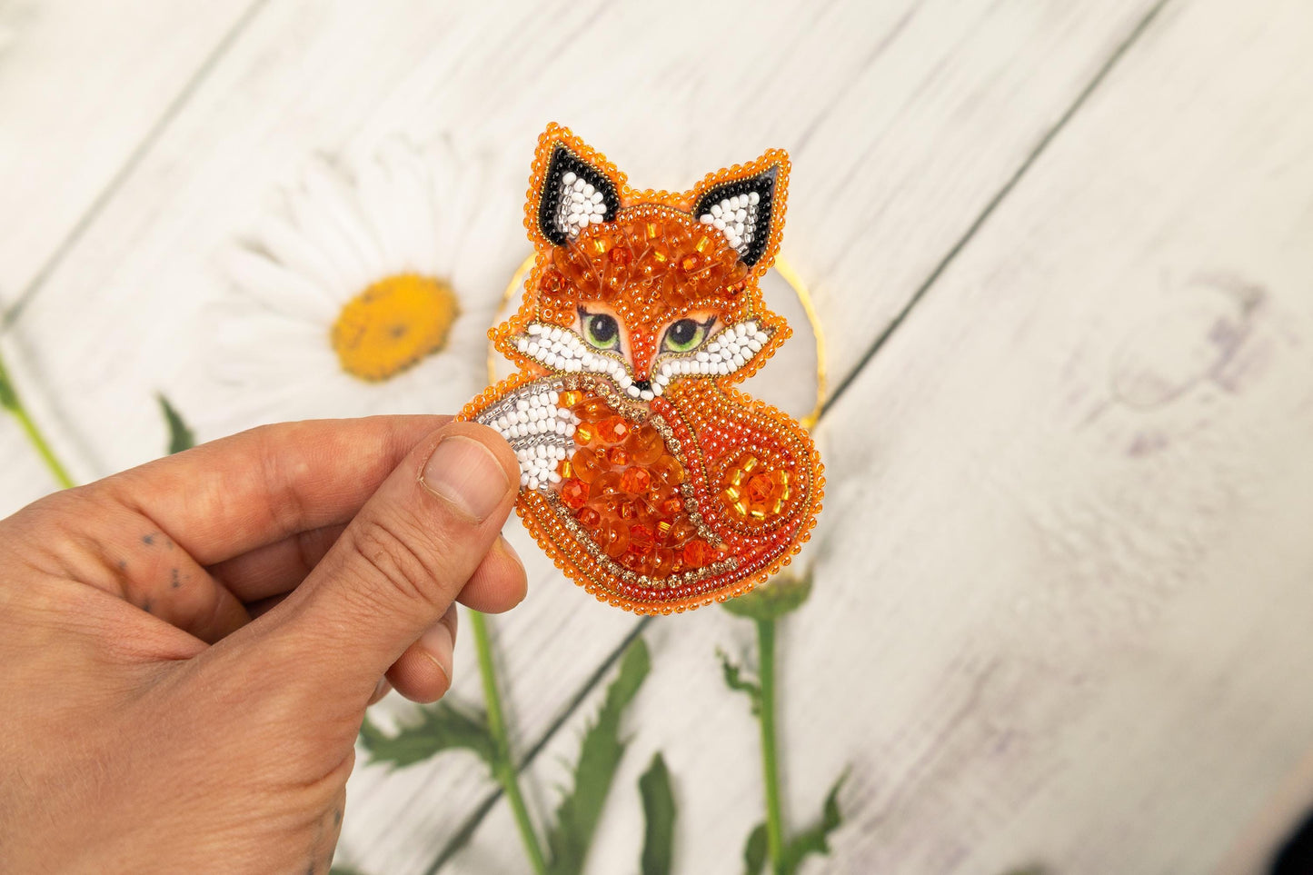 a hand holding a piece of beaded fabric with a fox on it