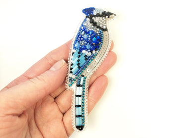 a hand holding a blue bird brooch in it&#39;s left hand