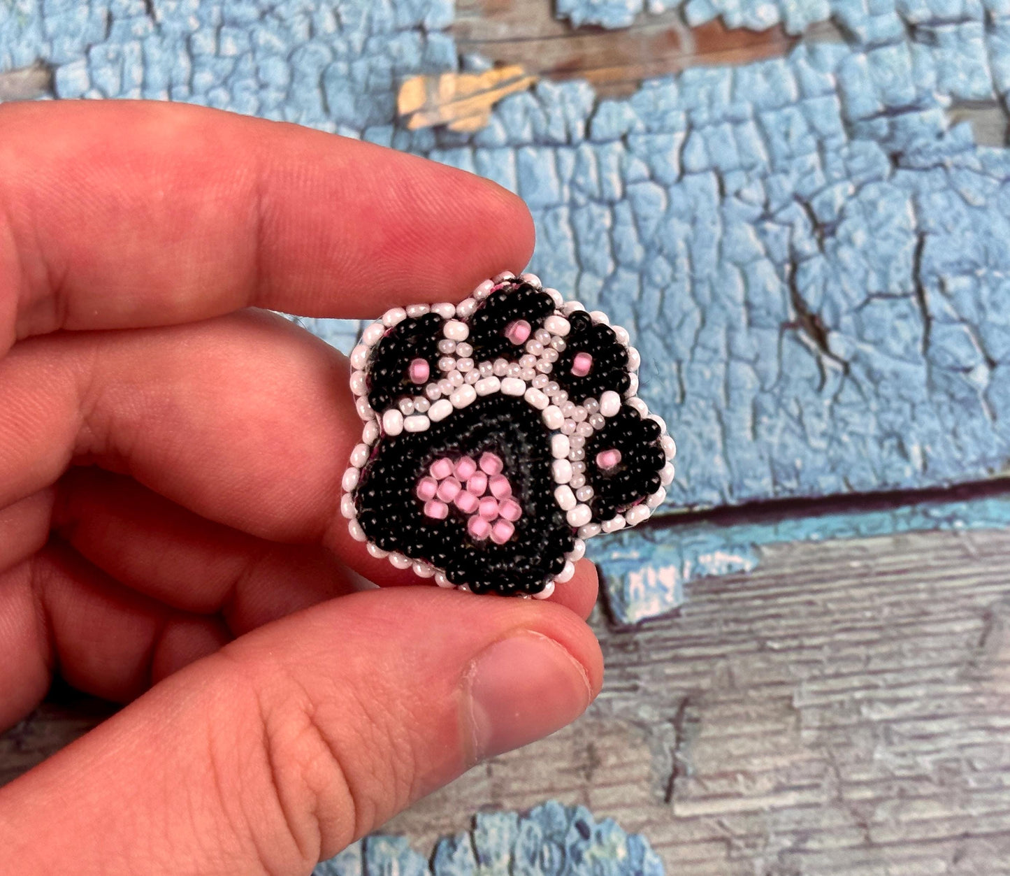 a hand holding a black and white beaded dog paw brooch