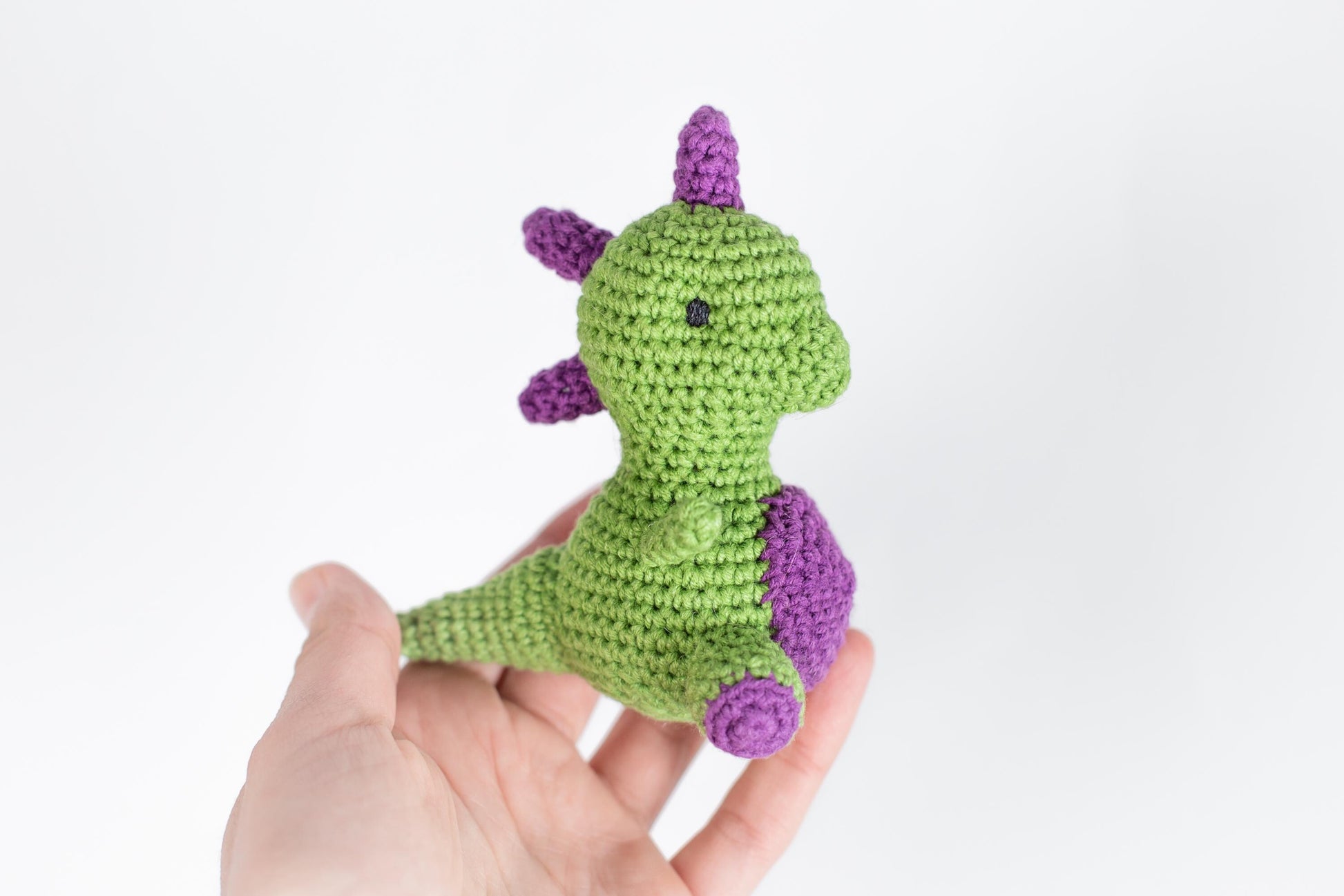 a hand holding a small crocheted green and purple toy