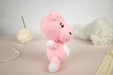 a pink crocheted teddy bear sitting next to a ball of yarn
