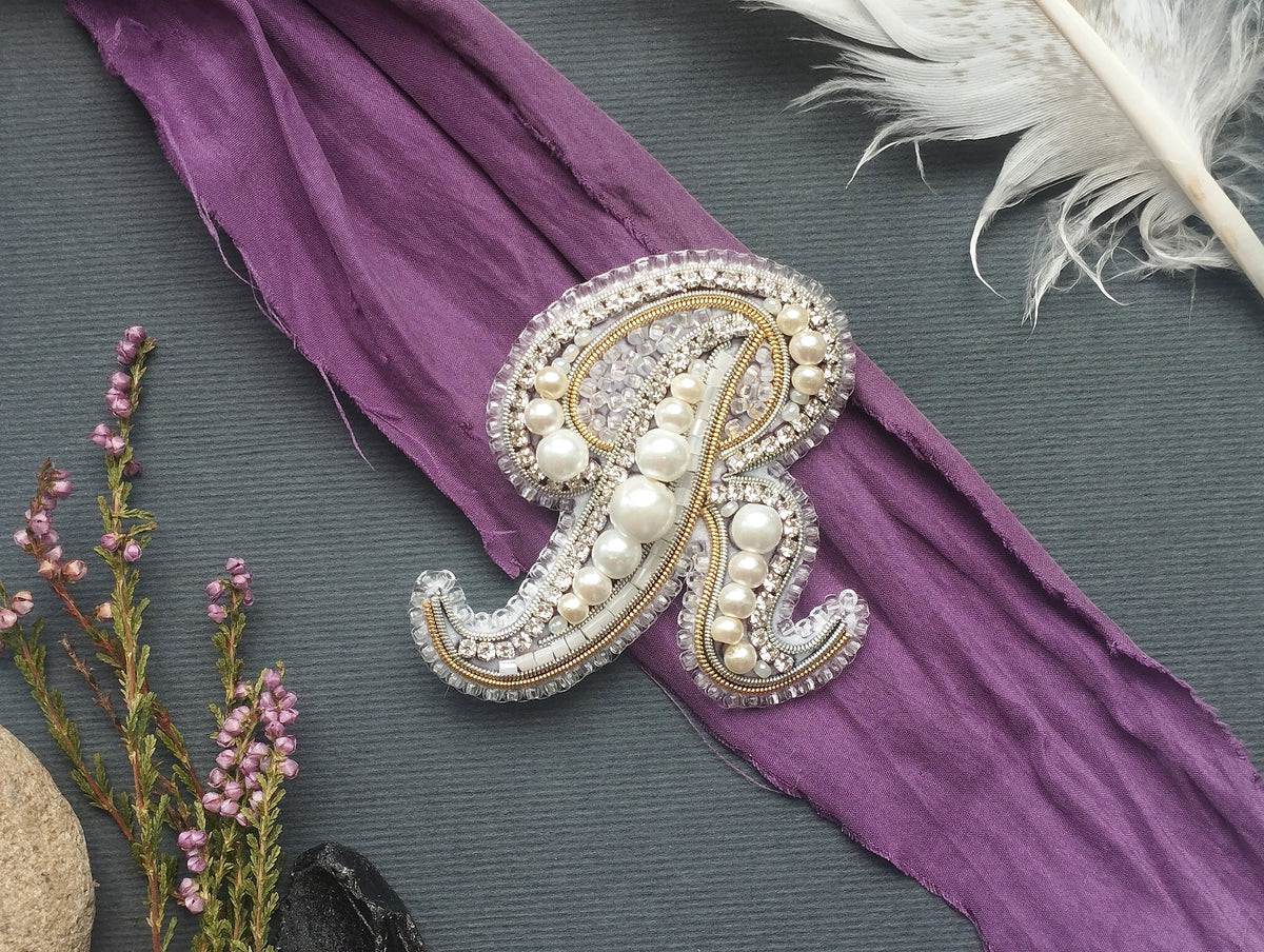 a decorative monogram made of pearls and jewels, placed on a purple fabric.