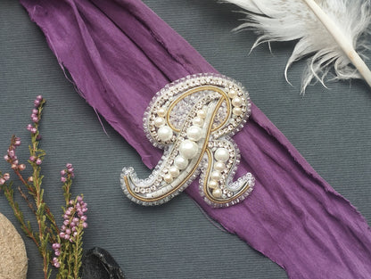 a decorative monogram made of pearls and jewels, placed on a purple fabric.