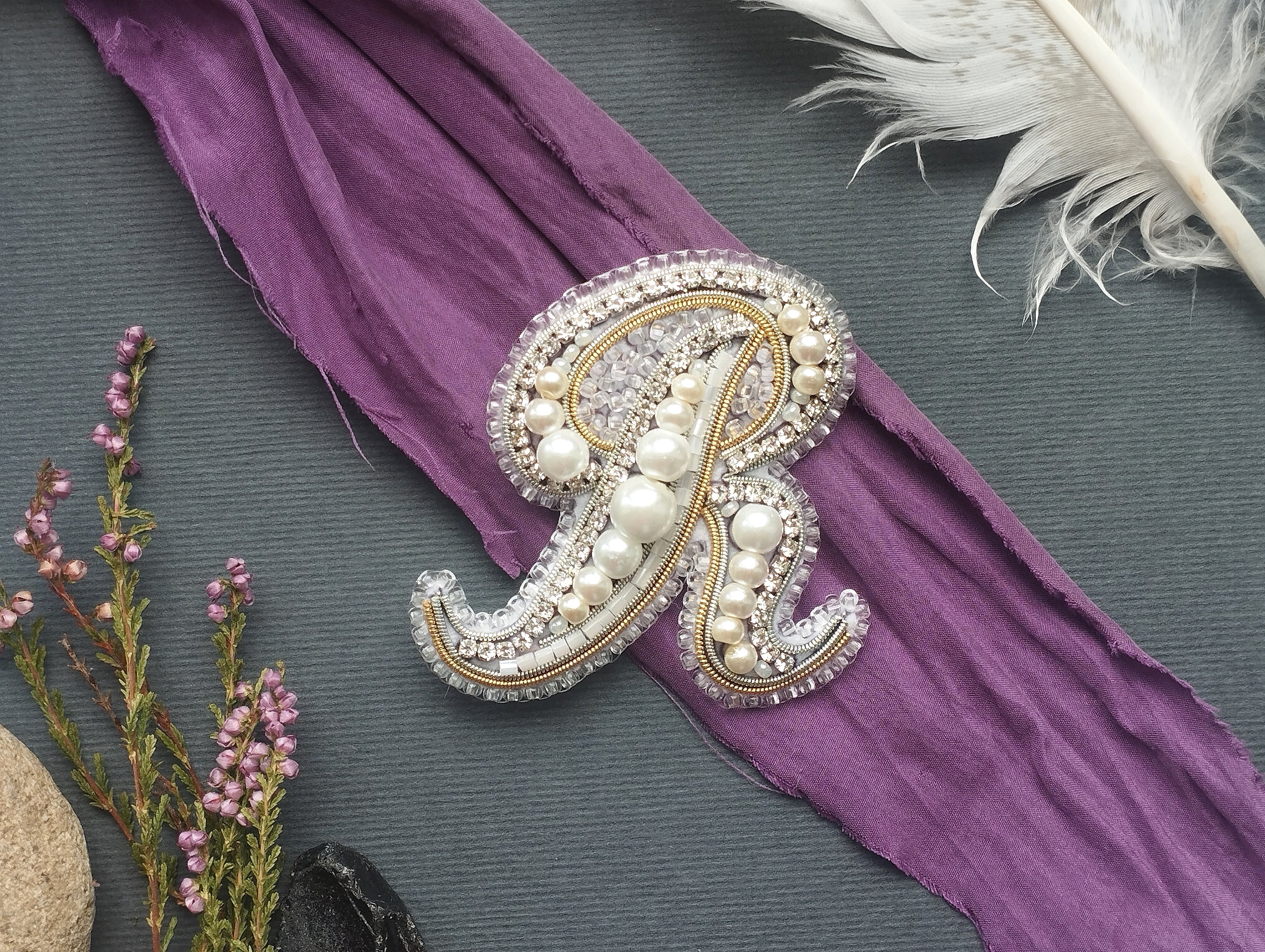 a decorative monogram made of pearls and jewels, placed on a purple fabric.