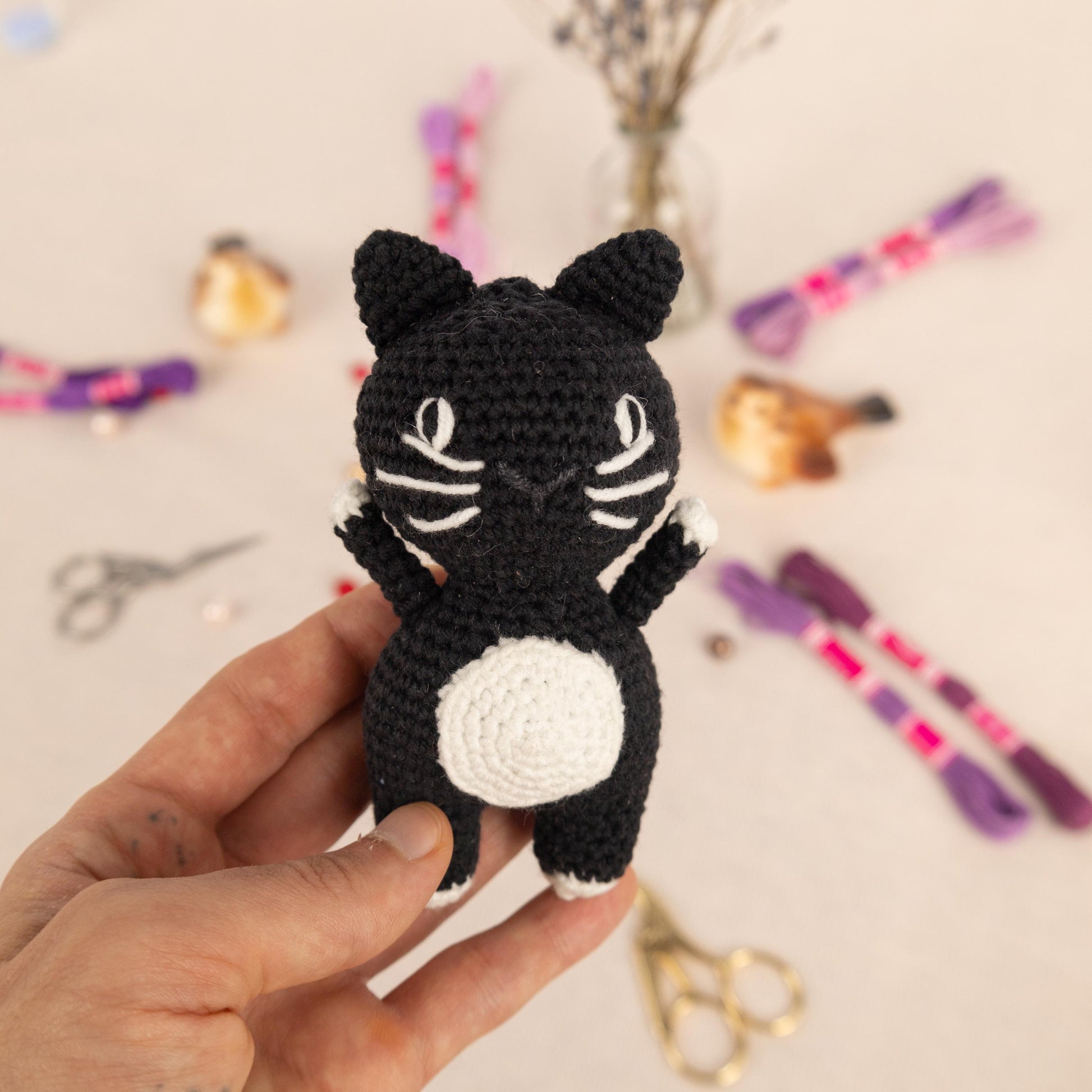 a hand holding a small crocheted black and white cat