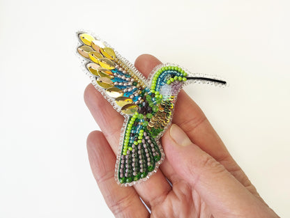 a hand is holding a beaded bird brooch