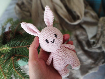 a hand holding a small pink crocheted bunny