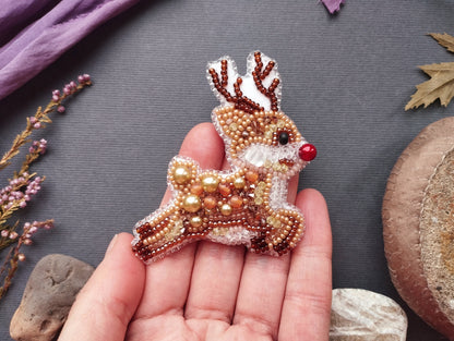 A hand holding a beaded reindeer brooch against a gray background.