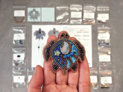 A hand holding a beaded turtle-shaped pendant against a background of various craft supplies and materials.