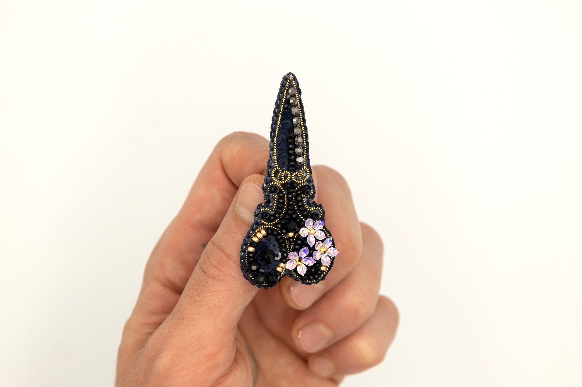 a hand holding a small black and gold brooch
