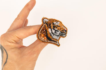 a hand is holding a beaded tiger brooch