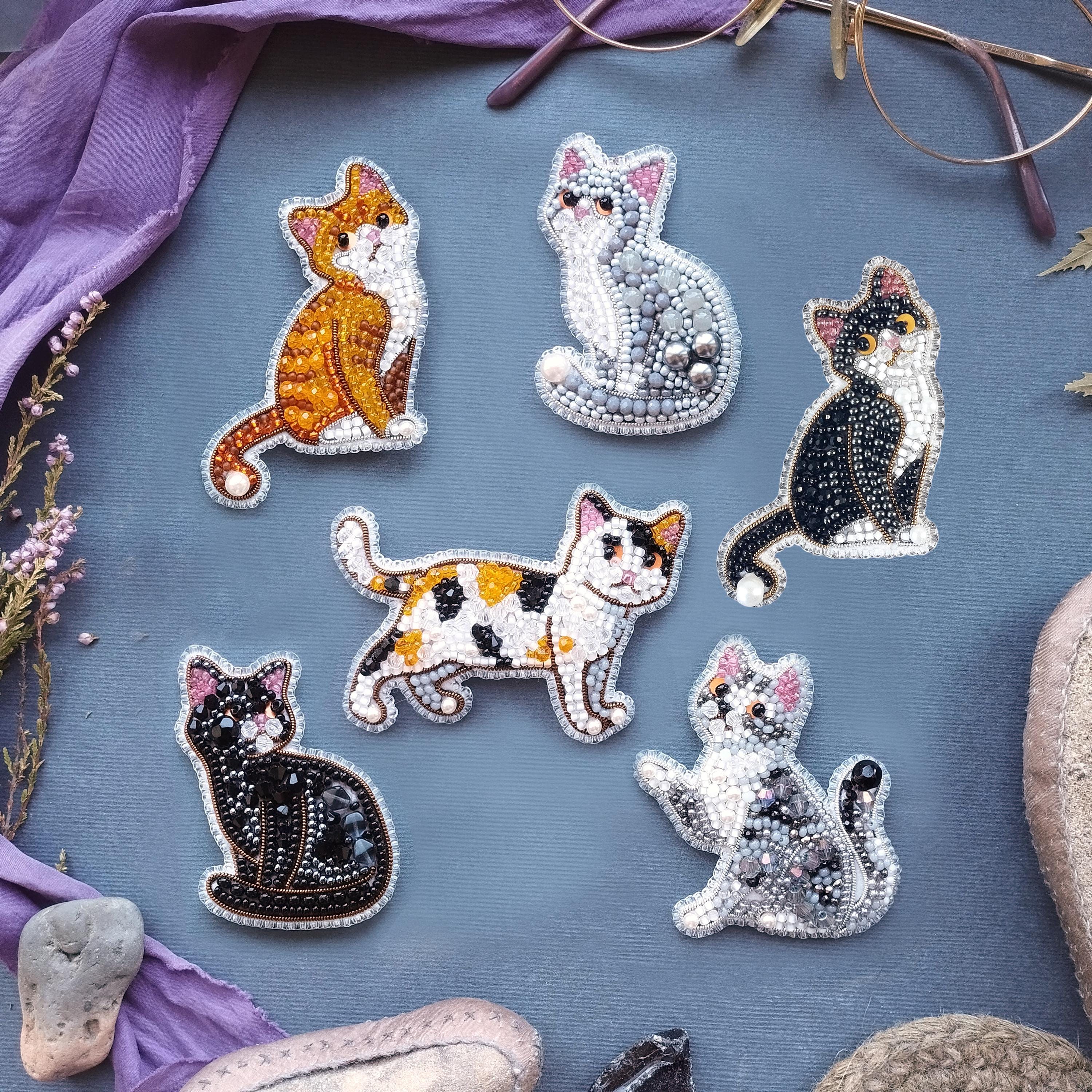 a collection of six cat-themed brooches or badges, each with a unique design and color scheme, arranged on a blue background.