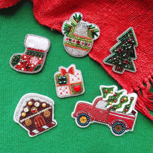 a collection of Christmas-themed embroidered or beaded decorations, including a Christmas tree, a gift box, a snowman, a truck, and a house, all set against a green background.