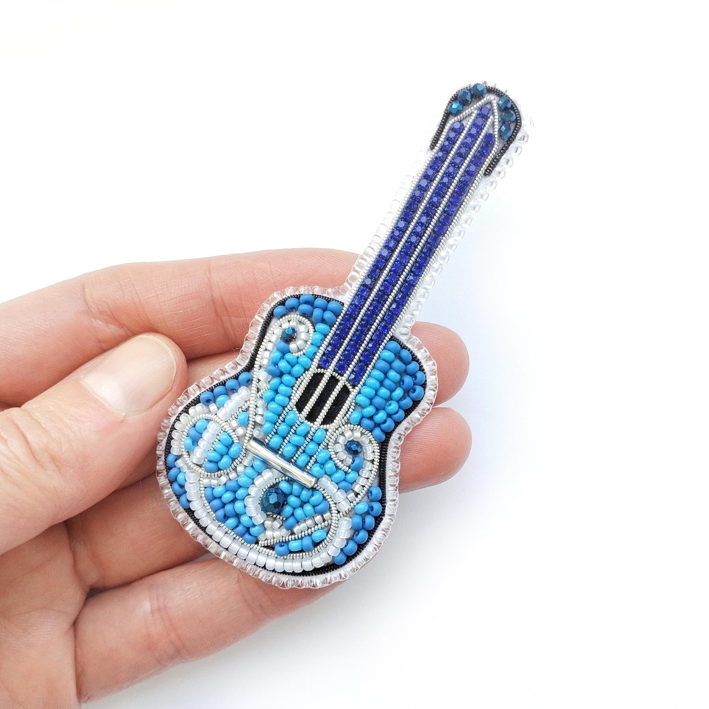 A hand holding a small, intricately beaded guitar-shaped object.