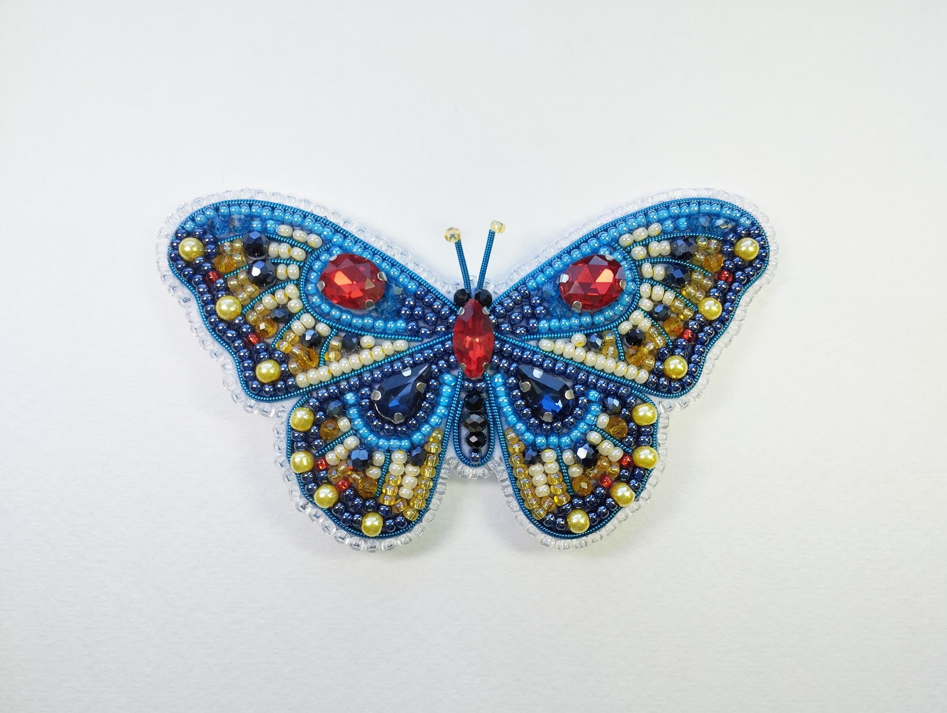 a beaded butterfly with red eyes on a white surface