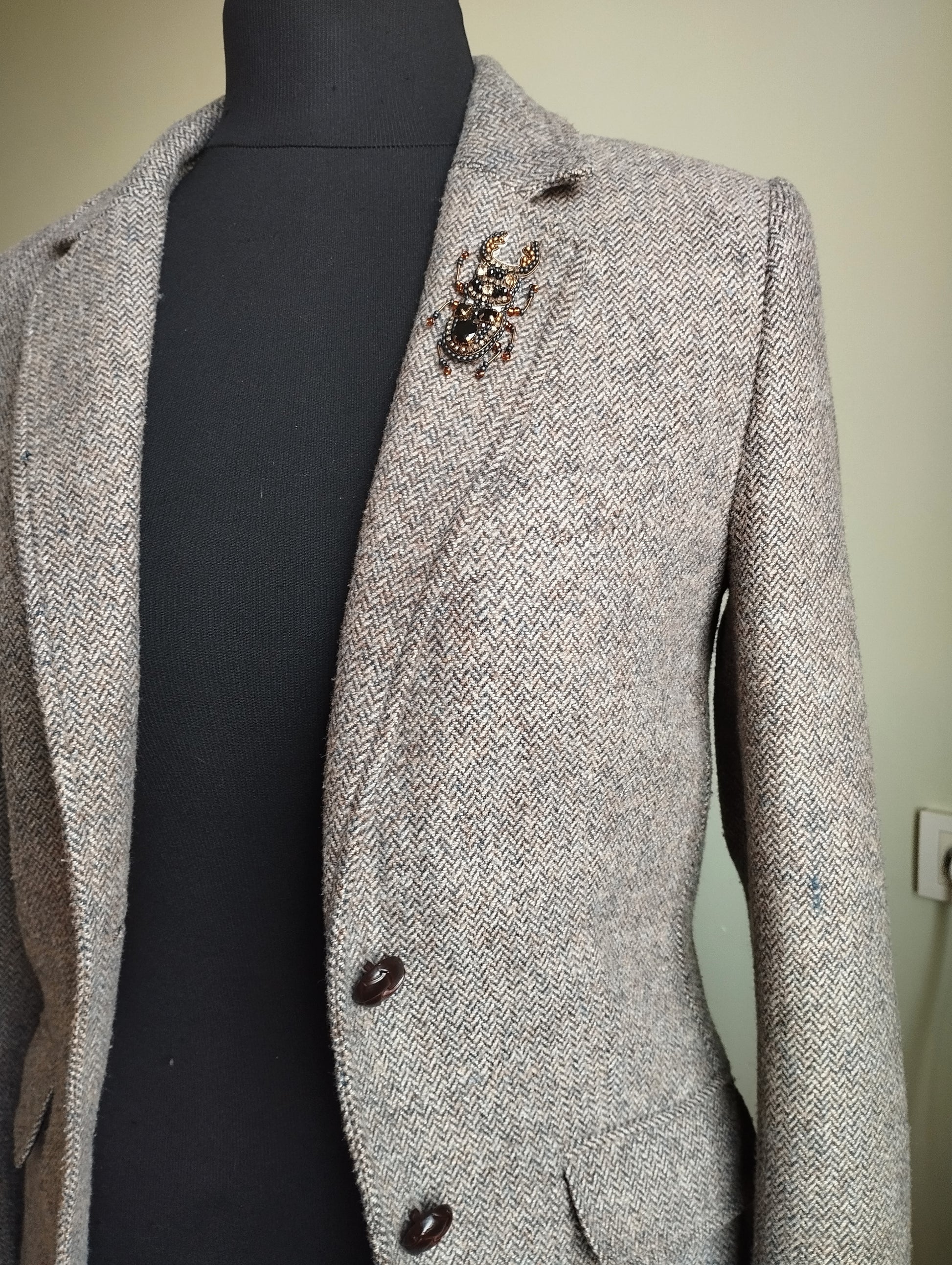 A gray tweed jacket with a black turtleneck and a decorative brooch on the left side of the jacket.