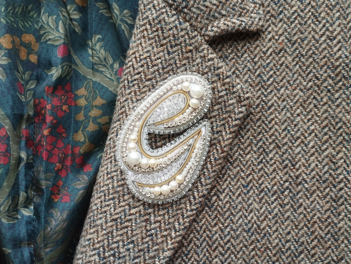 a close-up view of a decorative letter 'E' on a fabric surface, with a floral patterned fabric visible in the background.