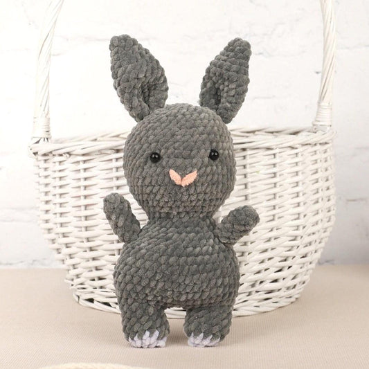 a gray knitted bunny sitting in front of a basket