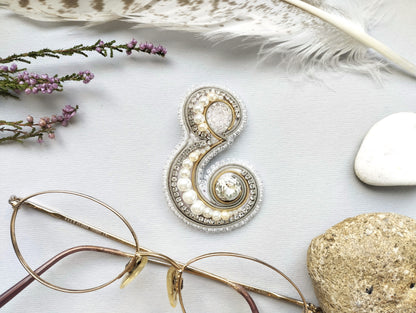 a close-up view of a pair of glasses, a decorative piece, and various natural elements such as feathers, rocks, and flowers arranged on a white background.