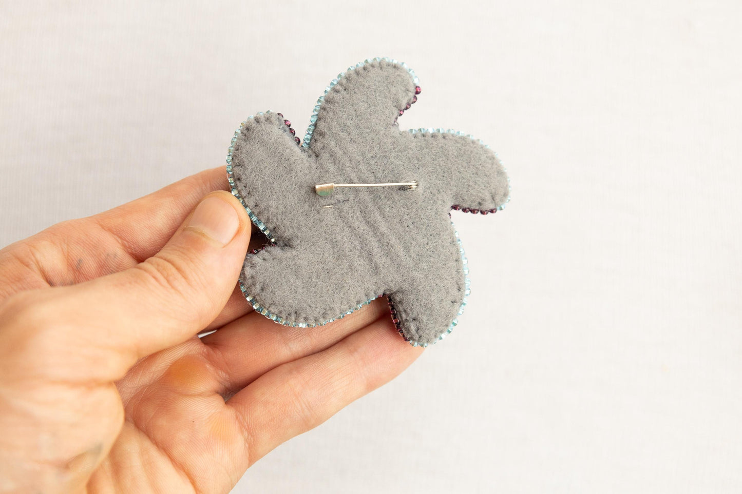 a person is holding a gray teddy bear brooch