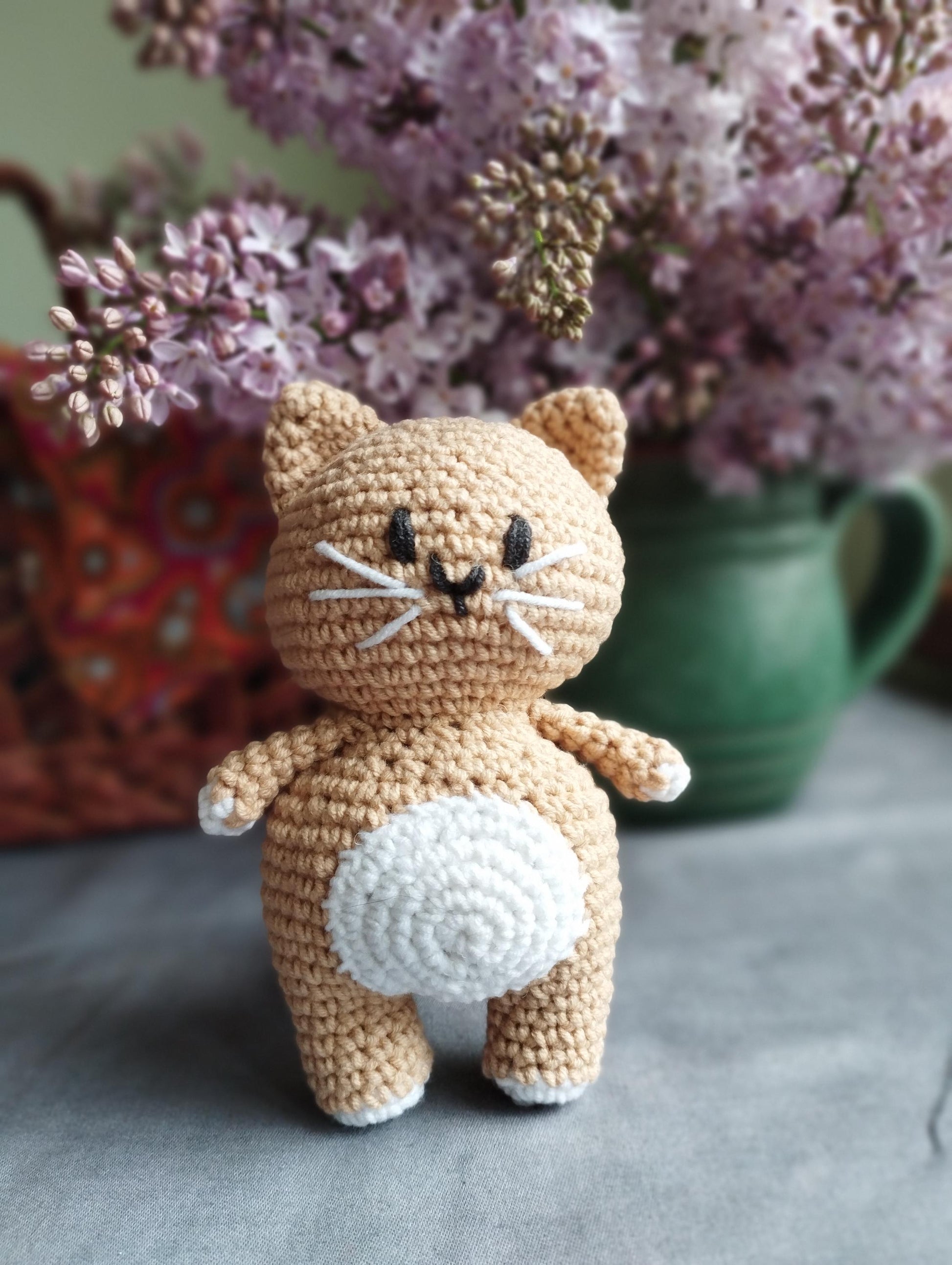 a crocheted cat sitting on a table next to a vase of flowers