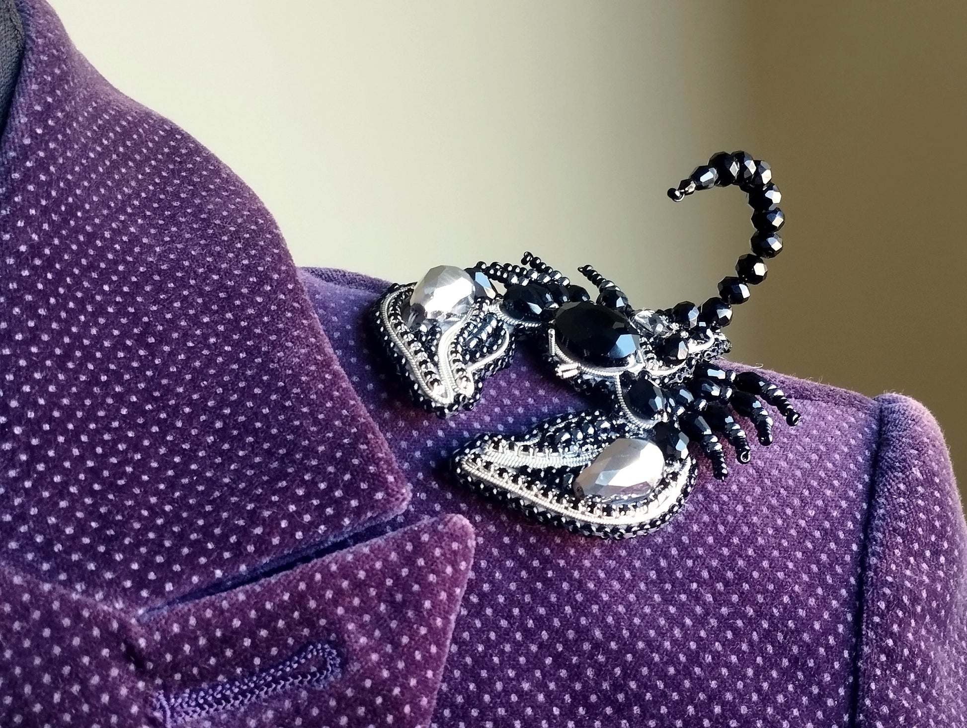 A close-up view of a purple velvet jacket with a decorative black and silver brooch featuring a spider-like design.