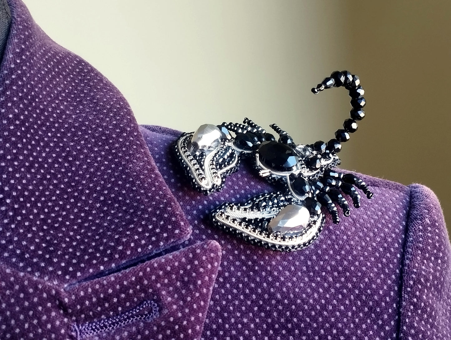 A close-up view of a purple velvet jacket with a decorative black and silver brooch featuring a spider-like design.