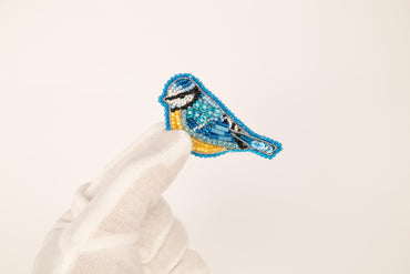 a hand is holding a small blue bird brooch