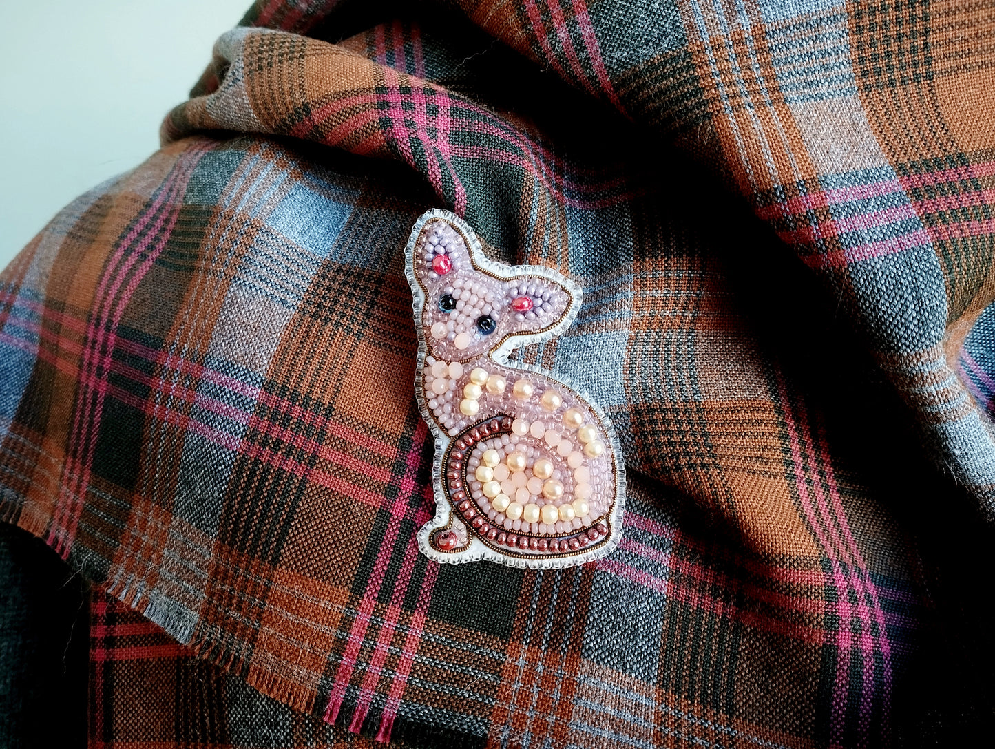 A close-up image of a decorative cat pin or brooch on a plaid fabric.