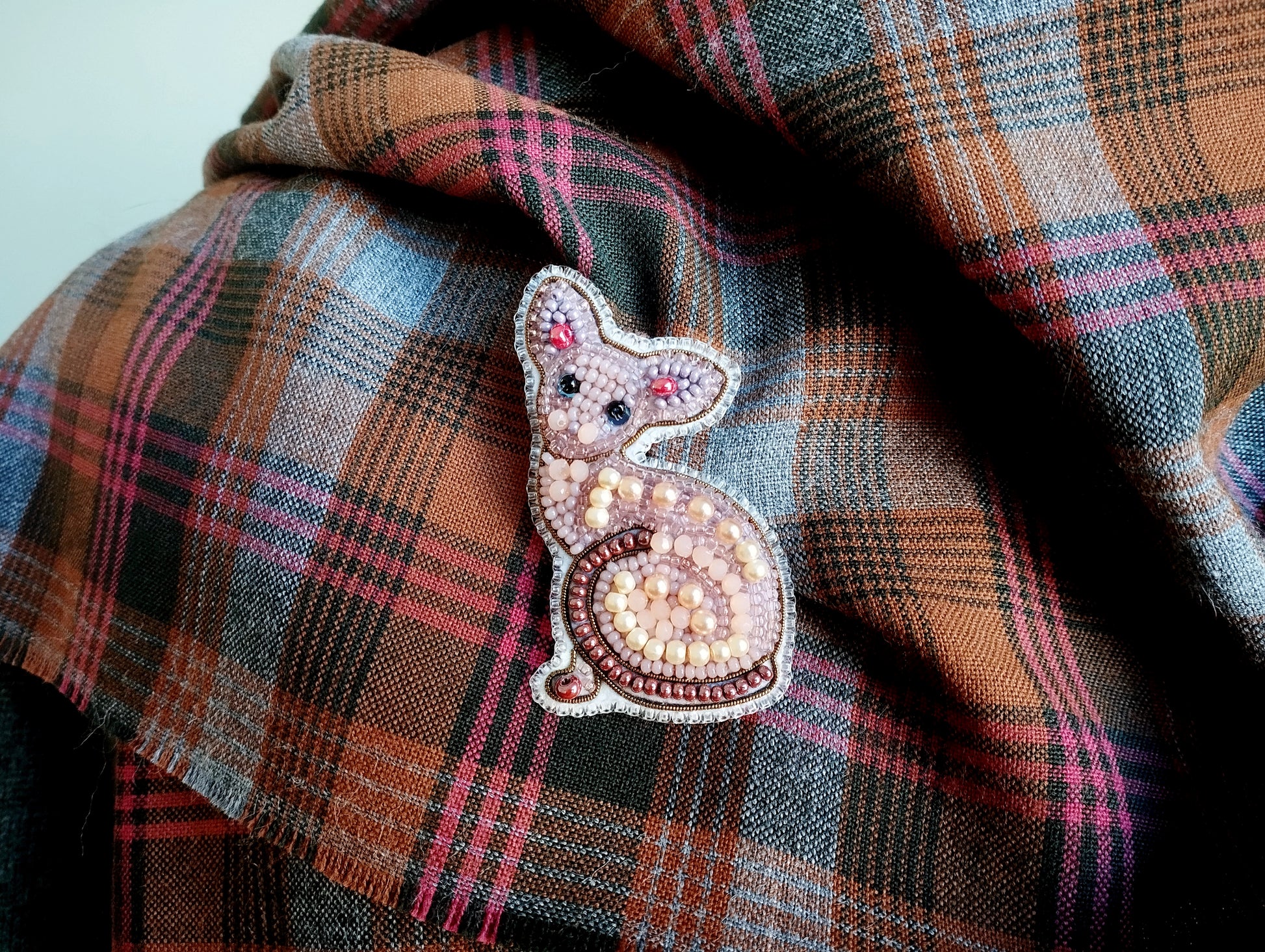 A close-up image of a decorative cat pin or brooch on a plaid fabric.