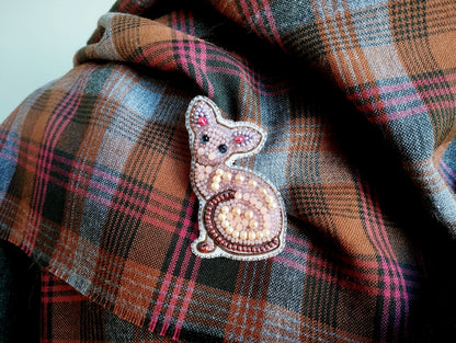 A close-up image of a decorative cat pin or brooch on a plaid fabric.