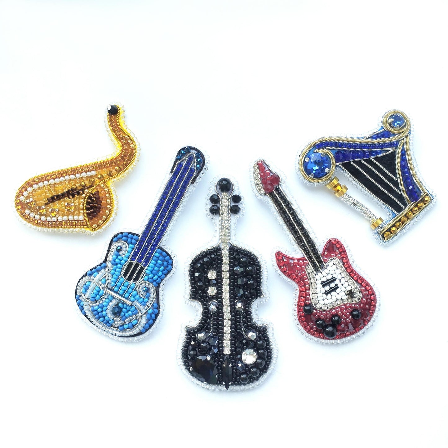 five ornate brooches or pins, each shaped like a different musical instrument and adorned with sparkling rhinestones or beads.